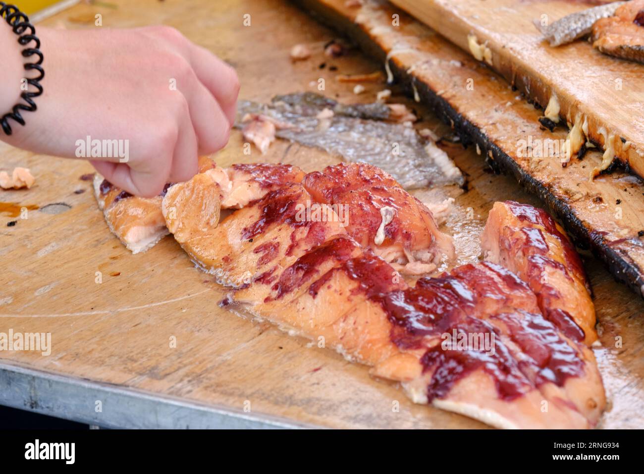 Hand eating Traditional Indigenous prepartation of salmon filet with maple sauce and berry sauce Stock Photo