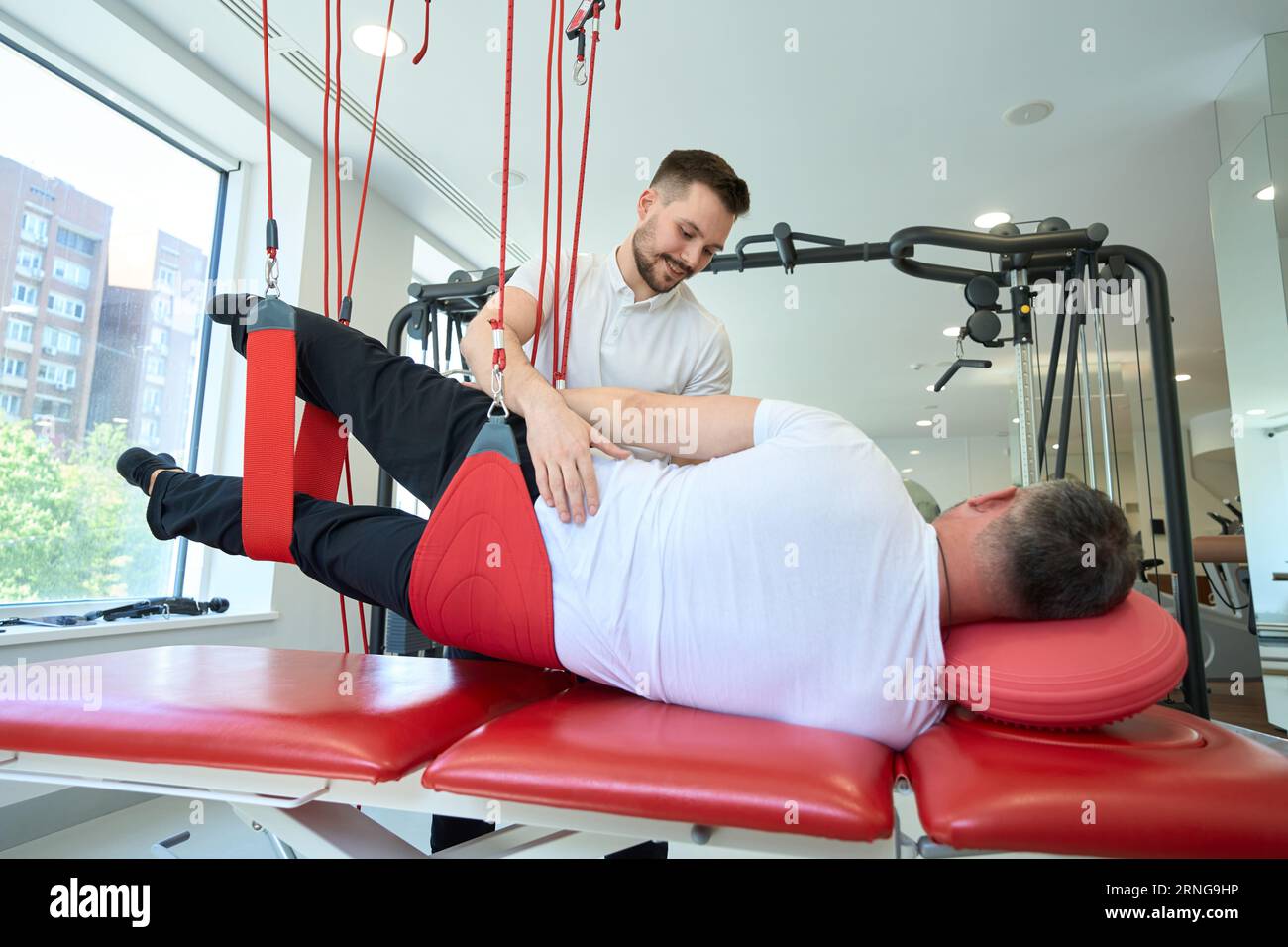 Professional kinesiotherapist rehabilitating patient using gym