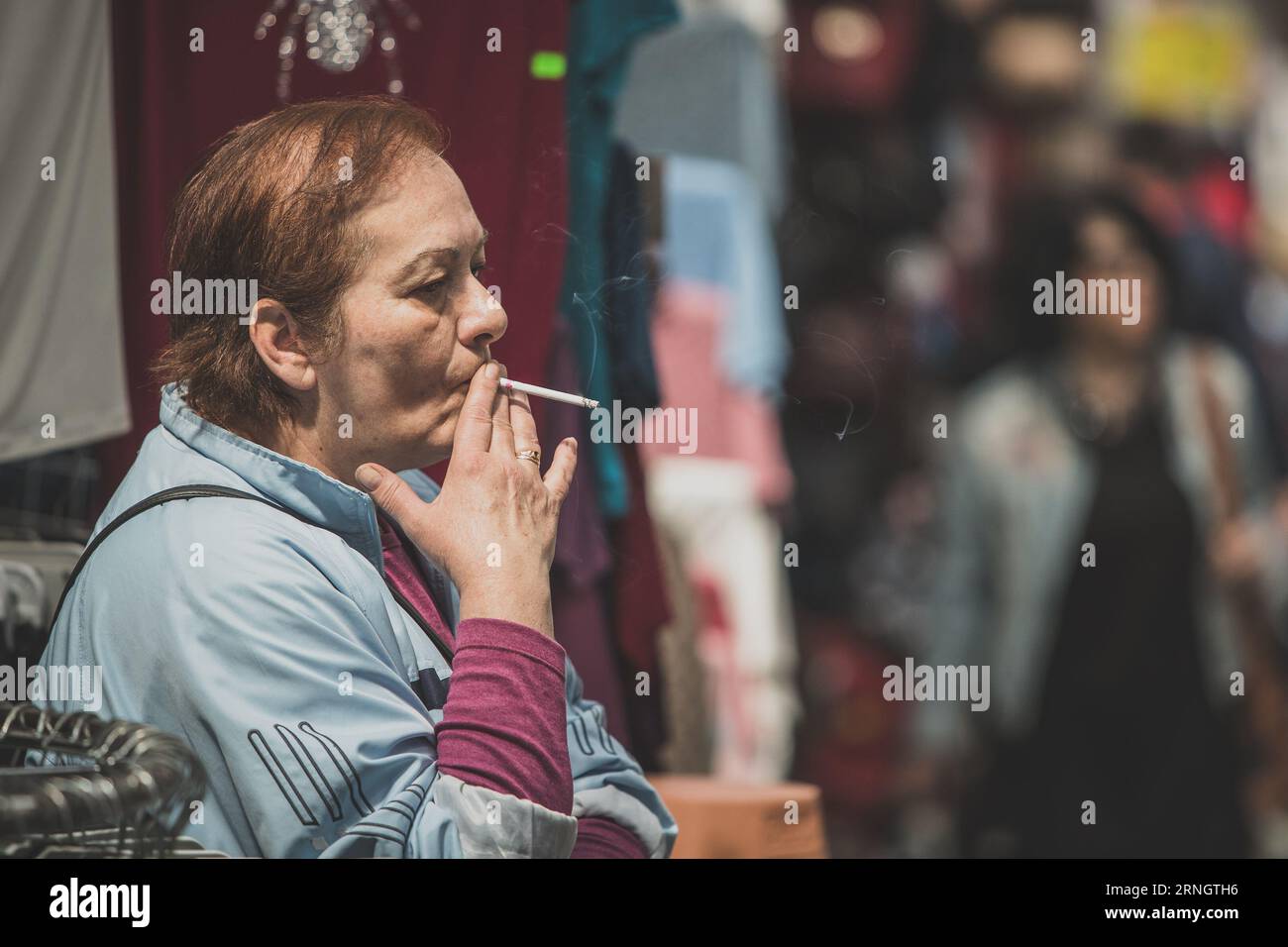 Banja Luka, Bosnia, 2.5.2019: Typical salesperson in the market of Banja  Luka, filled with goods, vegetables and shoes. Seller smoking a cigarette  Stock Photo