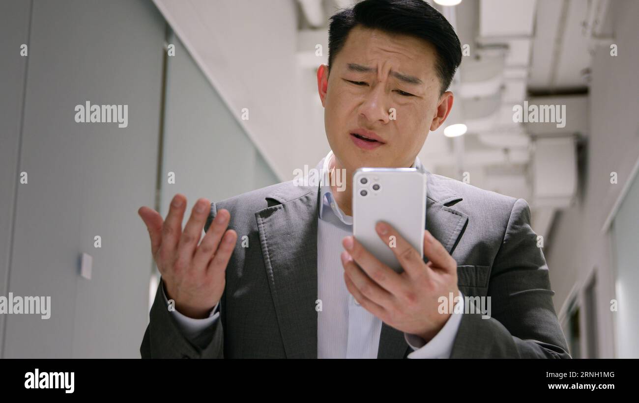 Frustrated upset Asian middle-aged man male chinese korean businessman employer read bad message on mobile phone worried crash debt bankruptcy loss Stock Photo