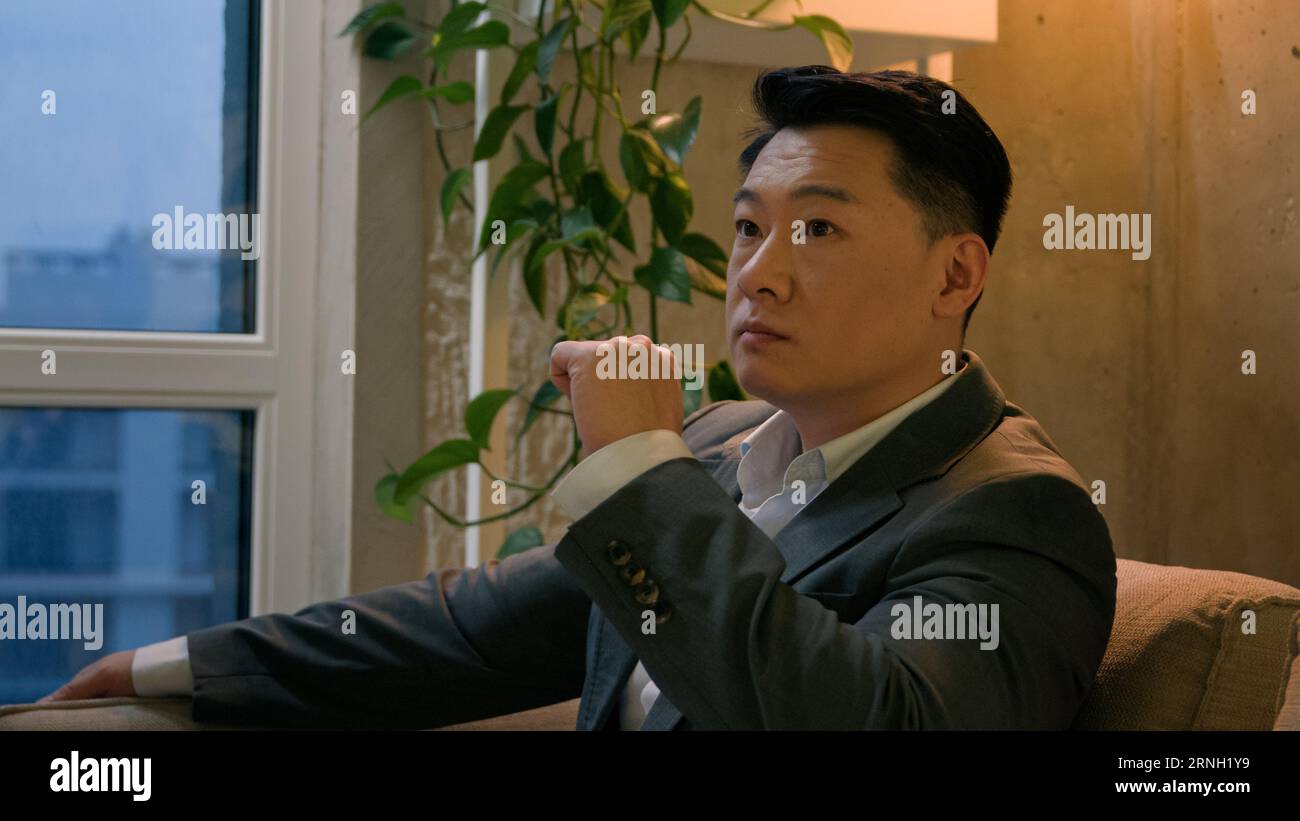 Doubtful thoughtful Asian chinese man think decision sit in office business center looking window korean male businessman puzzled pensive entrepreneur Stock Photo