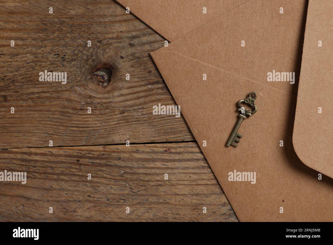 Paper envelopes and small key on wooden table, flat lay. Space for text