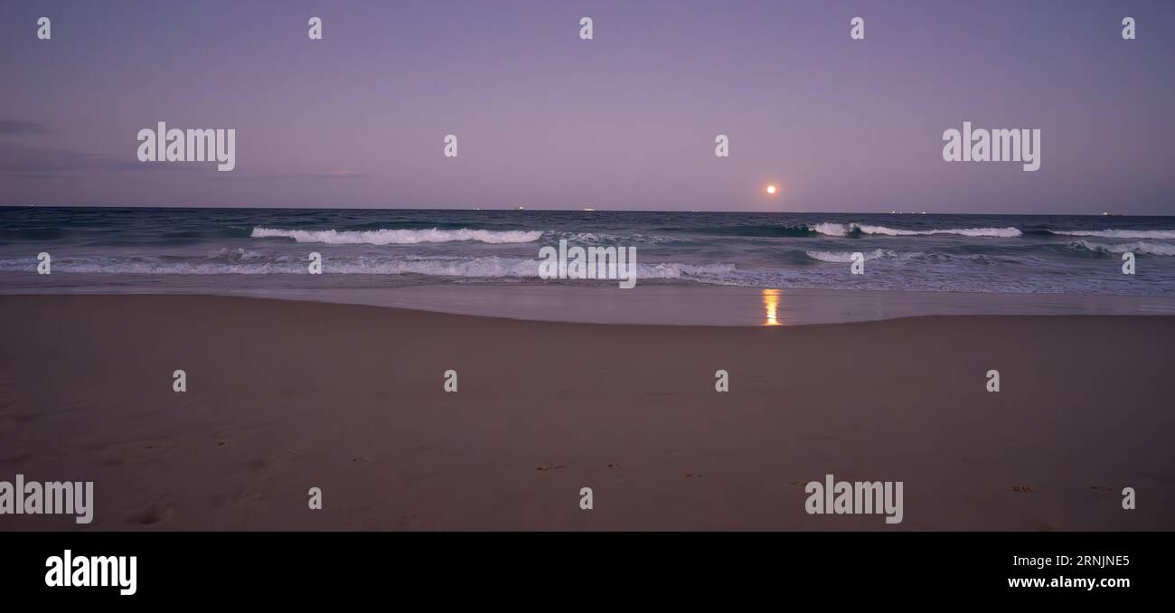 A blue moon, full moon, rising over the Pacific Ocean, Sunshine Coast, Eastern Australia at the end of August, 2023, with ships on the horizon and sur Stock Photo