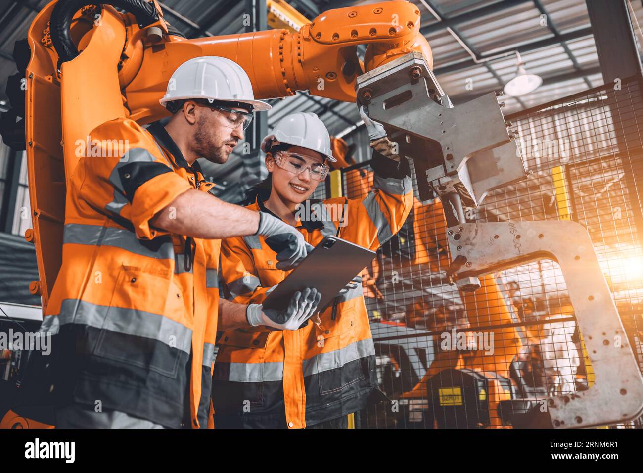 Engineer team service robot welding working in automation factory. People worker in safety suit work robotic arm software programming or replacing par Stock Photo