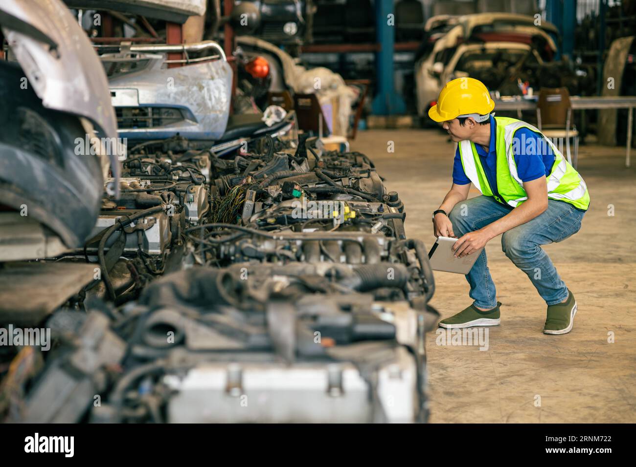 Engineer male worker check inventory store old used auto spare part engine gear part list for sale recycle in repair car garage market Stock Photo