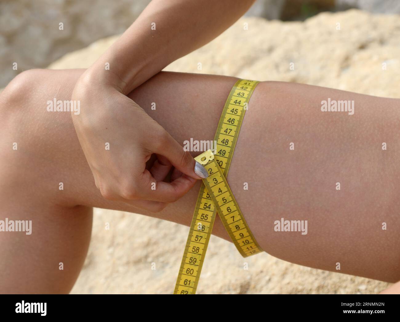 slender girl measuring her thigh with yellow meter Stock Photo