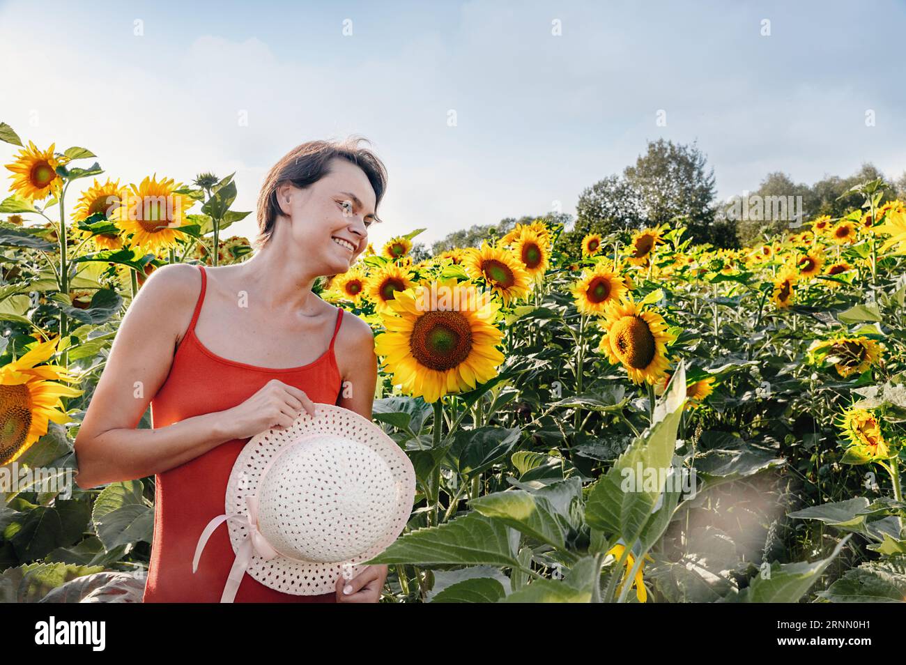 Beautiful woman posing in a field of sunflowers in a dress and hat. Fashion, lifestyle, travel and vacations concept. Stock Photo