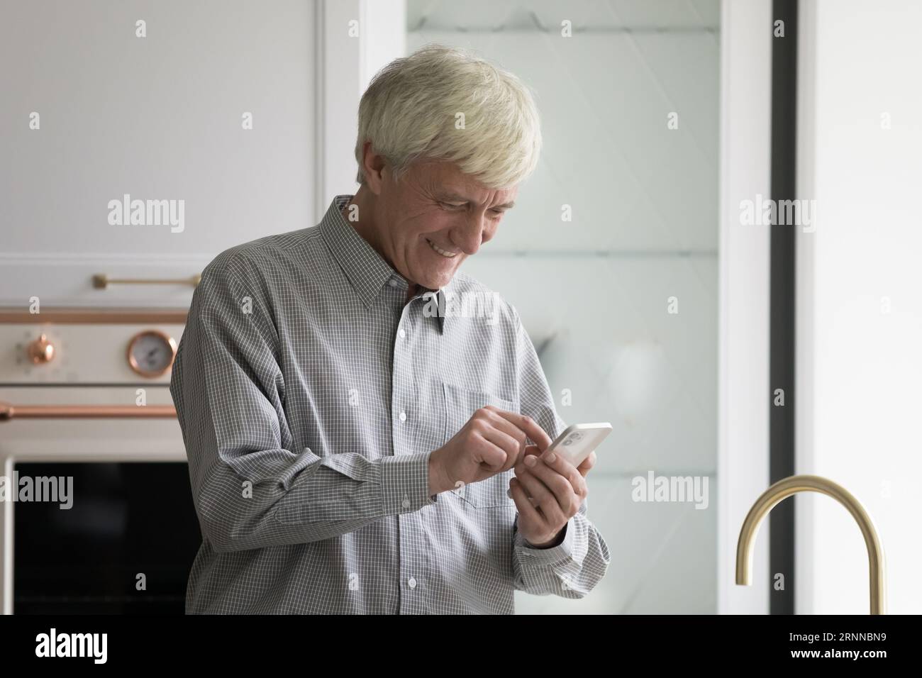Cheerful mature retired man using smartphone in kitchen Stock Photo