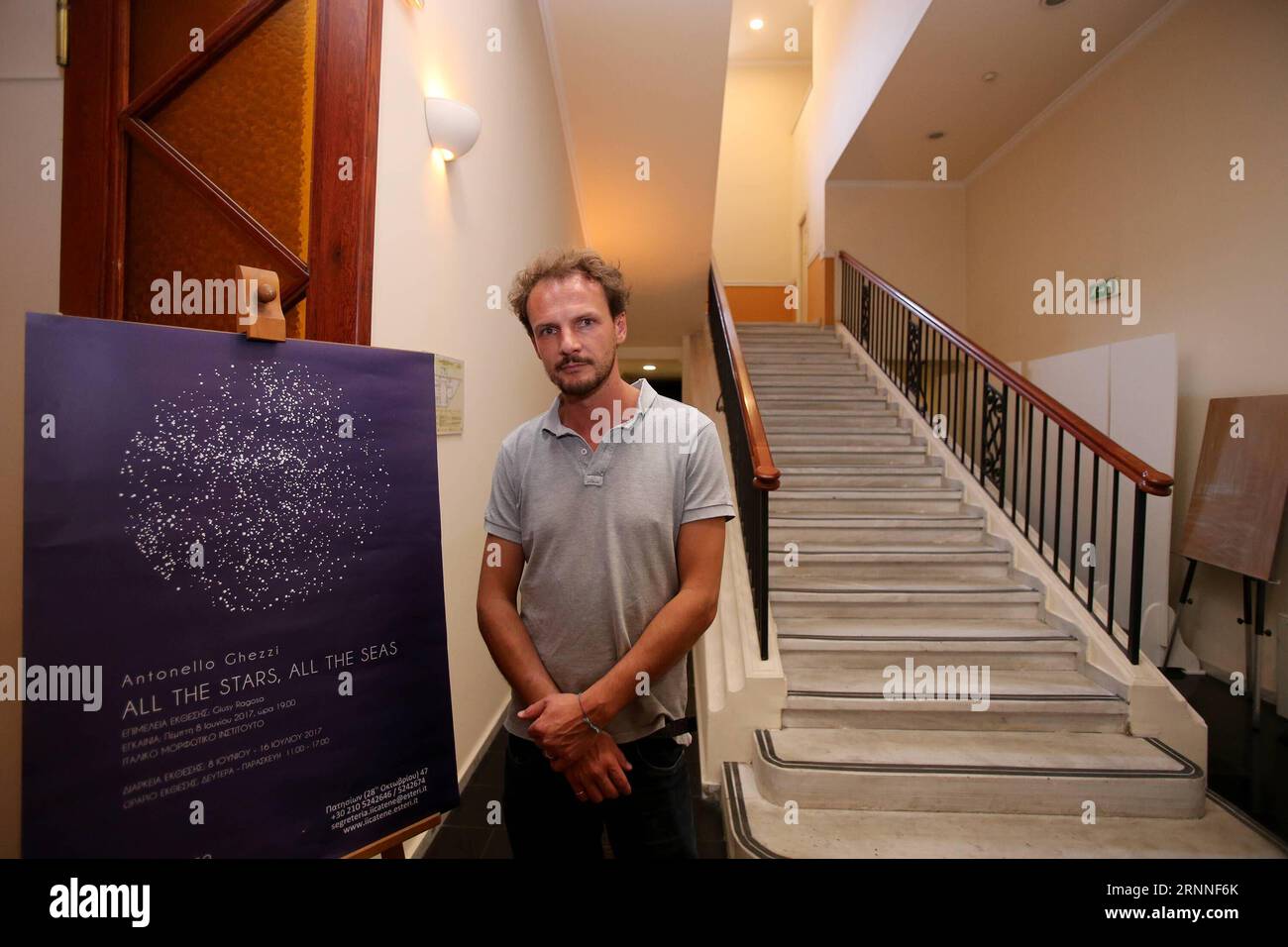 (170711) -- ATHENS, July 11, 2017 -- Photo taken on July 5 shows Italian artist Paolo Ghezzi at the entrance of the exhibition All the Stars, All the Seas in Athens, Greece. Two years into the crisis which has tested Europe, Italian art collective Antonello Ghezzi chose Greece, a country at the forefront of the mass influx of refugees and migrants, to launch their new project aimed to convey the message of unity and solidarity. The exhibition All the Stars, All the Seas is dedicated to the migrants and refugees, to all people adrift and to the fact that we are all united by the sea and the sky Stock Photo