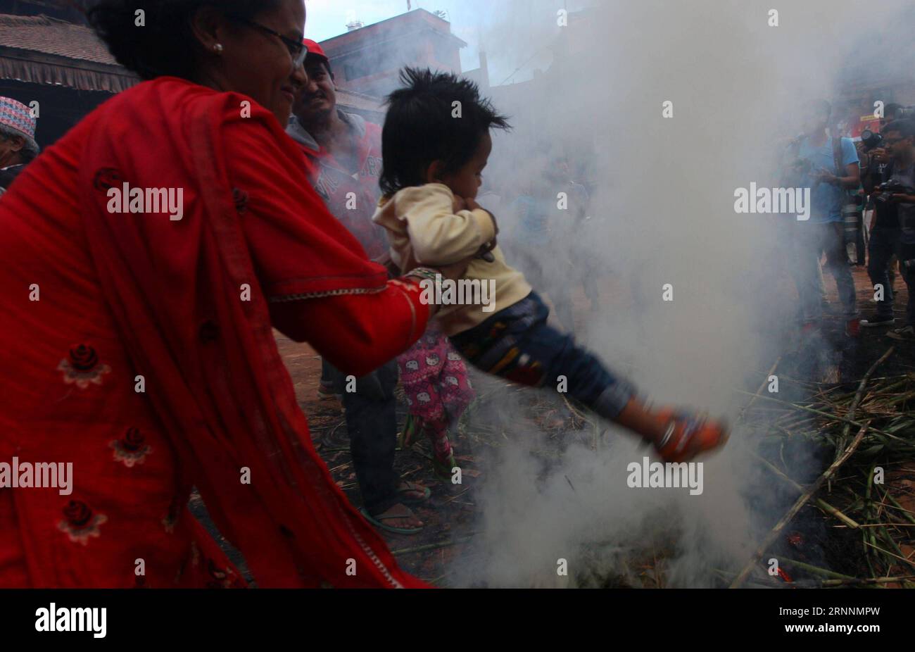 (170721) -- BHAKTAPUR, July 21, 2017 -- A woman carries her child above the fire after burning the dummy of Demon Ghantakarna in belief of removing evil spirits during the Ghantakarna Festival at Bhaktapur, Nepal, July 21, 2017. The Newar community of the Kathmandu Valley observe Ghantakarna, a festival to chase away evil spirits and usher in good fortune. People wear metal rings to safeguard against all ills and evil spirits. ) (dtf) NEPAL-BHAKTAPUR-GHANTAKARNA FESTIVAL sunilxsharma PUBLICATIONxNOTxINxCHN   Bhaktapur July 21 2017 a Woman carries her Child above The Fire After Burning The Dumm Stock Photo
