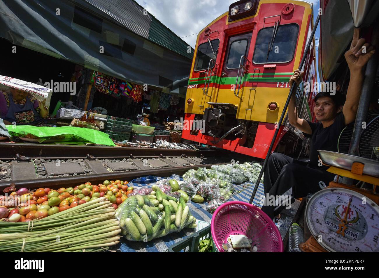 Bilder des Tages (170821) -- MAEKLONG, Aug. 21, 2017 -- A commuter train runs through Maeklong Market in central Thailand s Samut Songkhram Province, Aug. 19, 2017. In Maeklong Market, built along a railway track, a compromise is reached between vendors and passing commuter trains. When the rail track is clear, stall owners can set up stalls at will; yet eight times per day, the awnings and some of the goods have to be moved back from the rail and make way for arriving and departing trains. The business style around train timetables has made Maeklong Market one of the most unique markets in Th Stock Photo