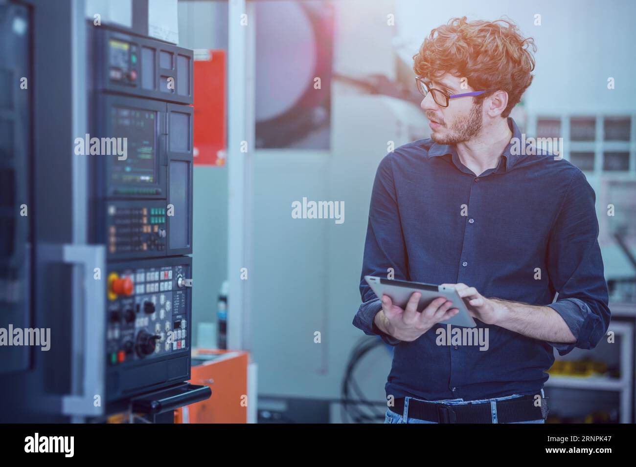 Professional young engineer factory worker programming CNC milling machine with a tablet computer. Stock Photo