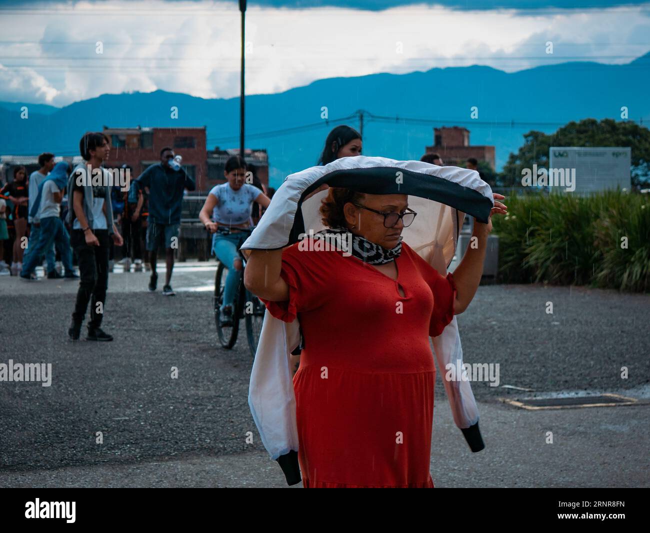 Medellín, Medellin, Antioquia, Colombia - May 28 2023: Colombian Woman Dressed in Red Walks Covering her Head from the Rain in a Public Park Stock Photo