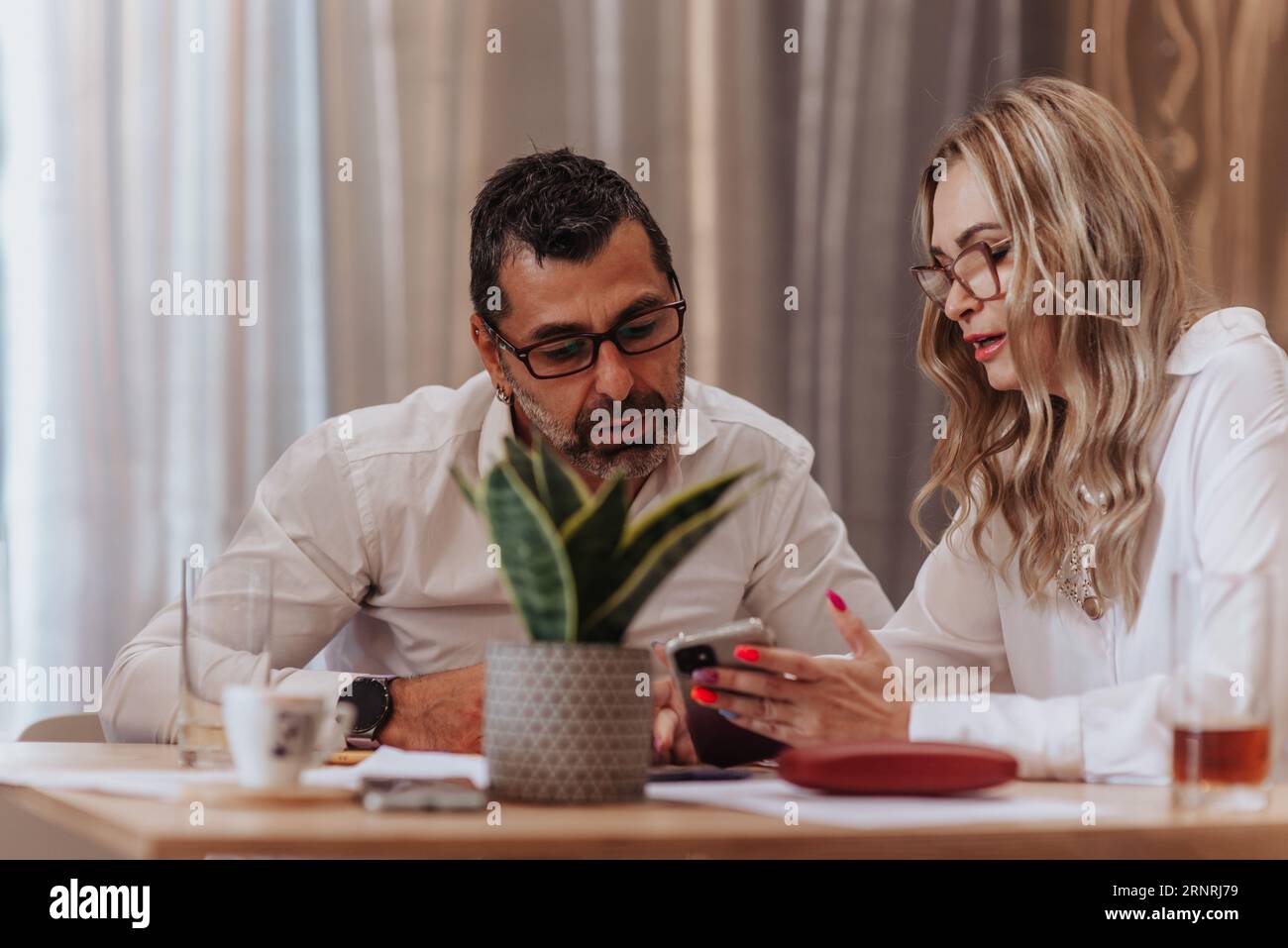 Two middle-aged business leaders discussing company work efficiency and profit growth while sitting at the cafe Stock Photo