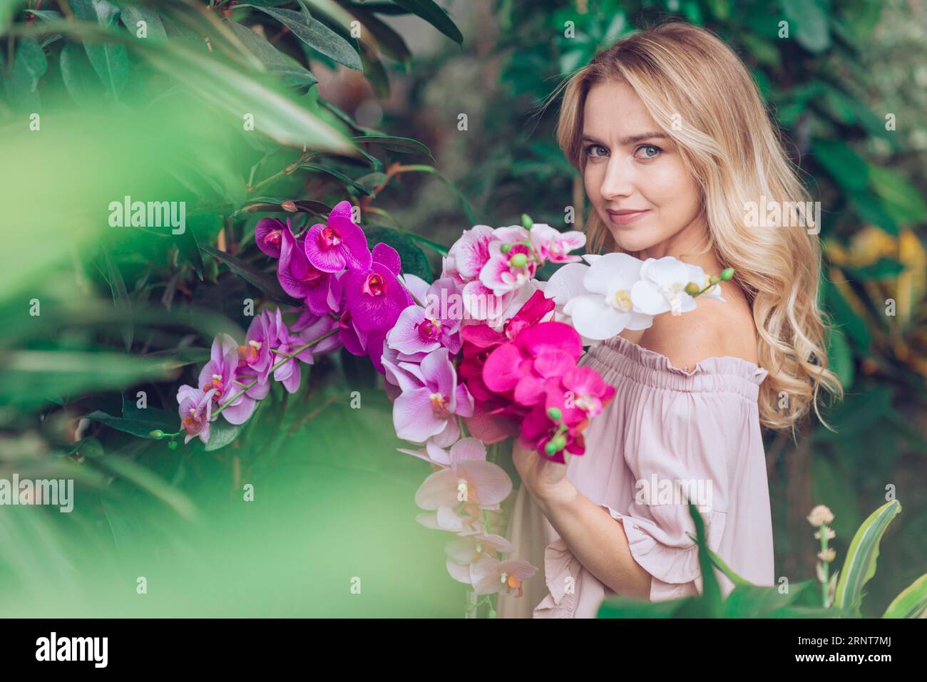 Blonde young woman standing garden holding orchid Stock Photo - Alamy