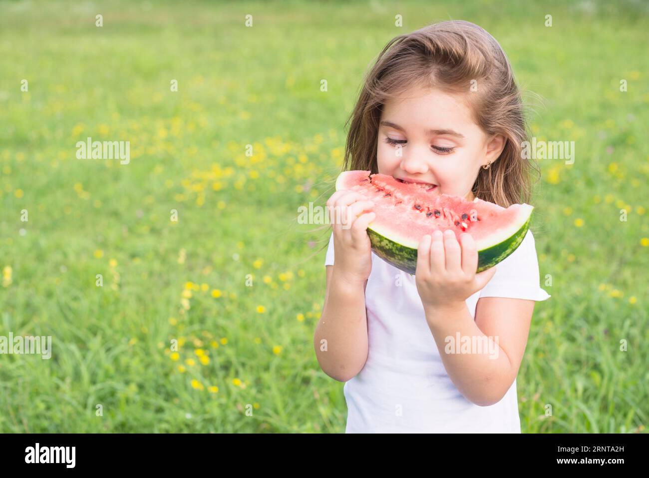 Little girl standing field eating red slice watermelon Stock Photo