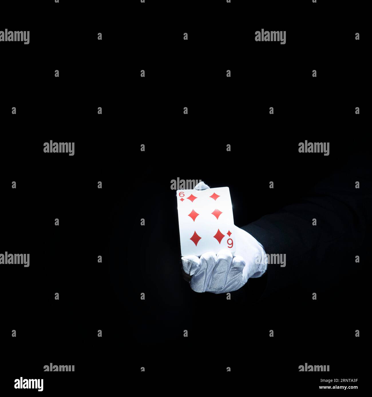 Magician s hand showing diamond playing card against black background Stock Photo