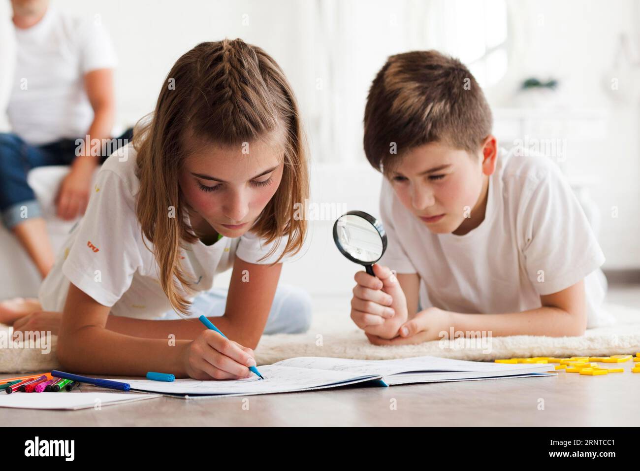 Boy looking through magnifying glass during his sister drawing book Stock Photo