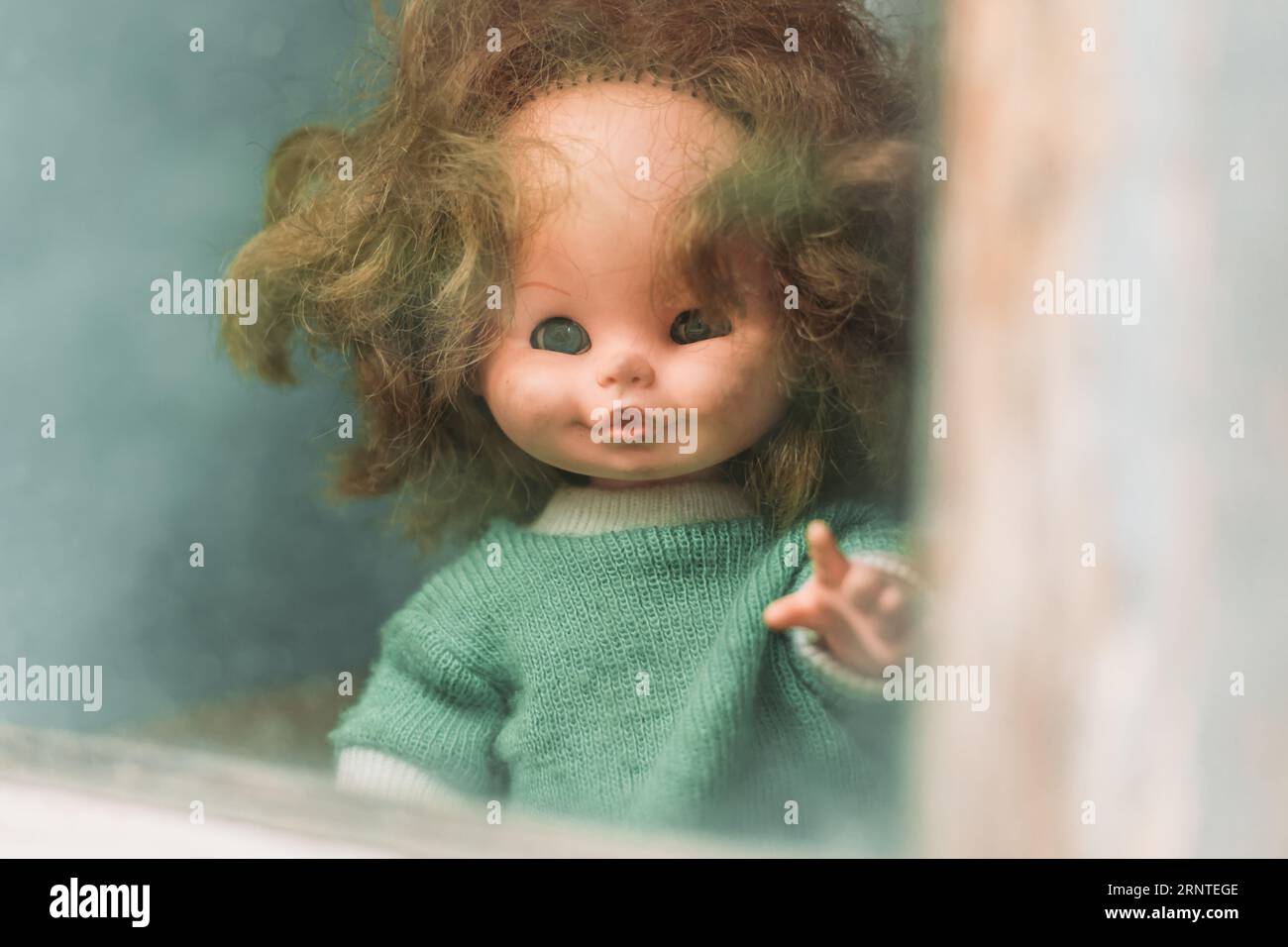 Close-up of an old doll peeking through the window. Halloween concept Stock Photo