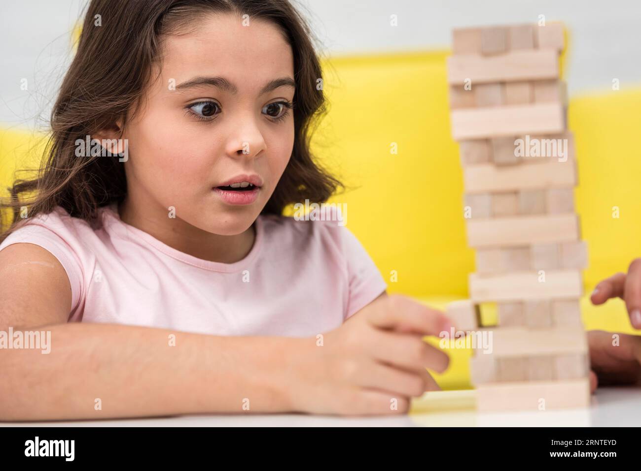 Little girl taking care while getting piece wooden tower game Stock