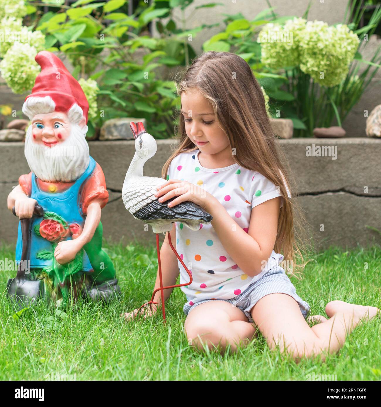 Girl sitting green grass playing with statue Stock Photo