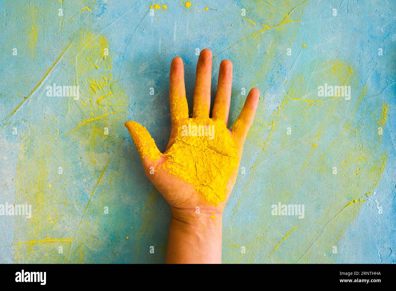 Yellow powder person s palm against painted messy wall with color Stock Photo