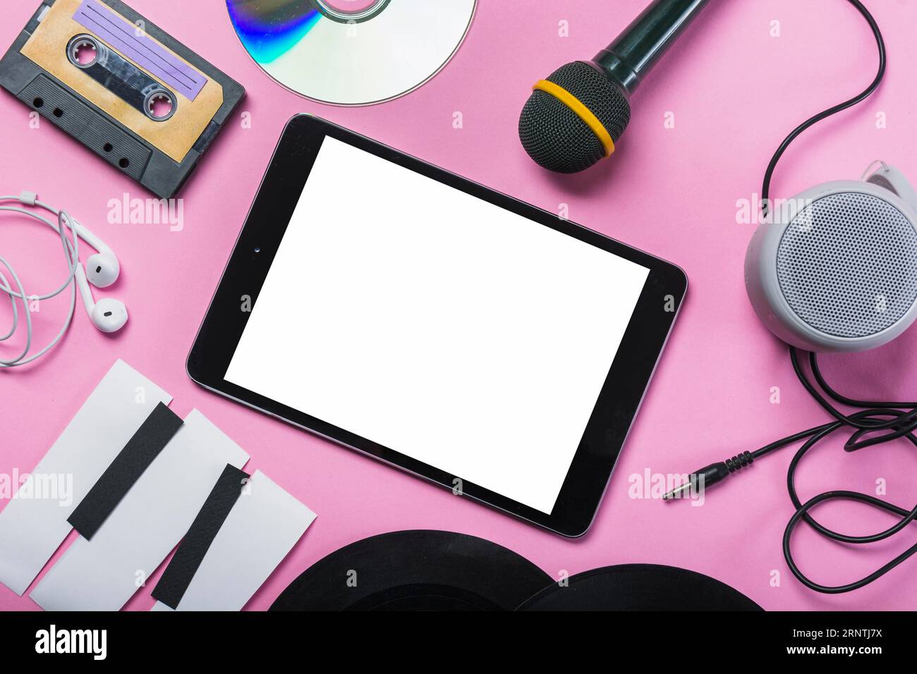 Cassette tape cd earphone vinyl record microphone speaker paper piano keys around digital tablet pink background Stock Photo