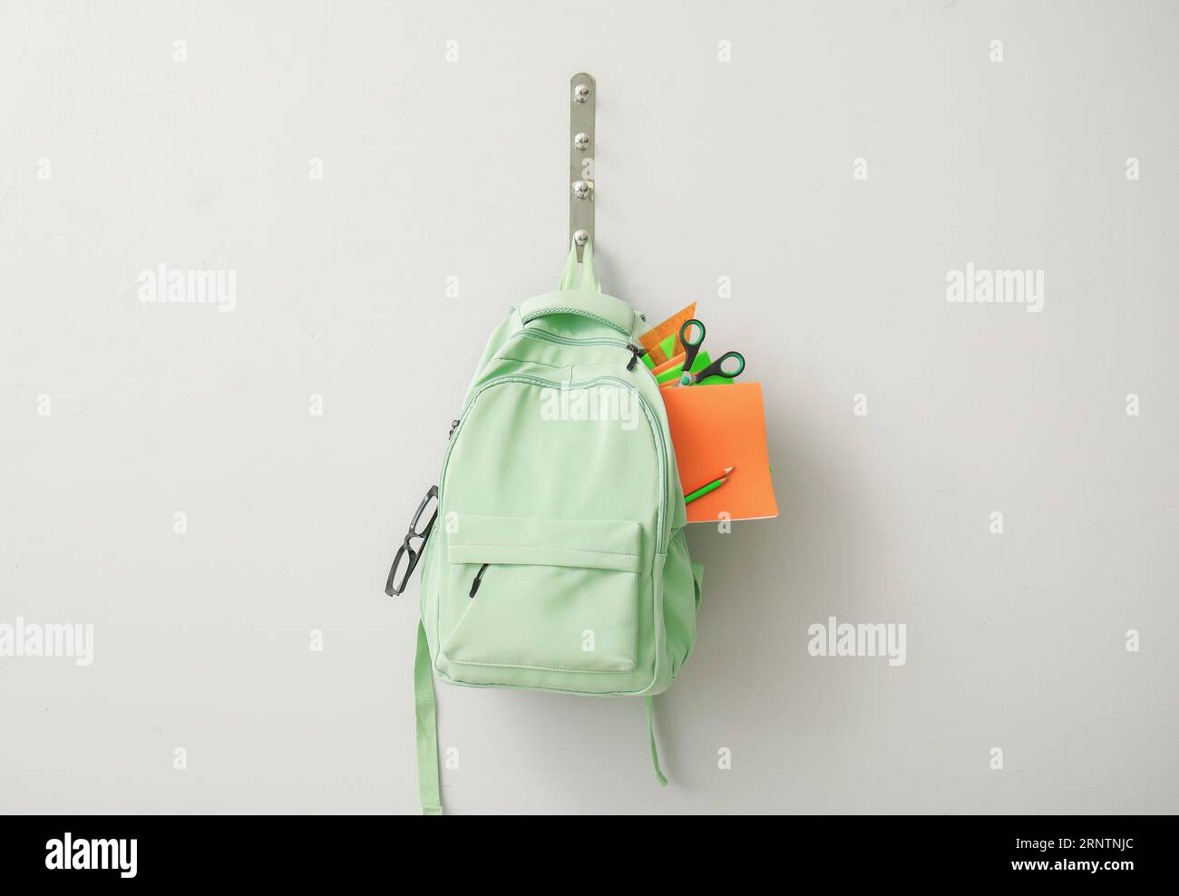 School backpack with different stationery hanging on light wall Stock Photo