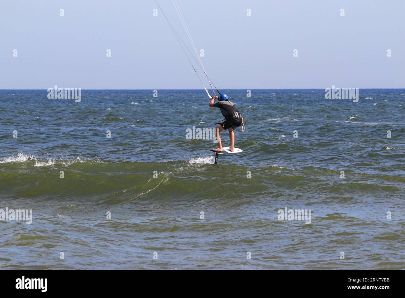 Rear view of a man kiteboarding in the Atlantic Ocean going over a small wave as he works his way further out. Stock Photo