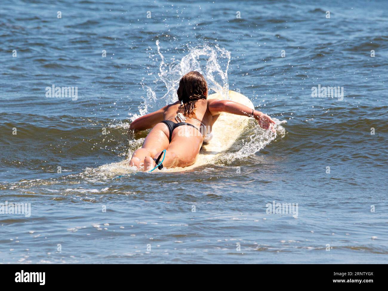 Rear view of a teenage girl wearing a bikini lying down on a surfboard