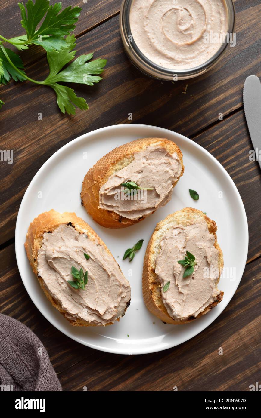 Toasted bread with chicken liver pate on plate over wooden background. Top view, flat lay Stock Photo