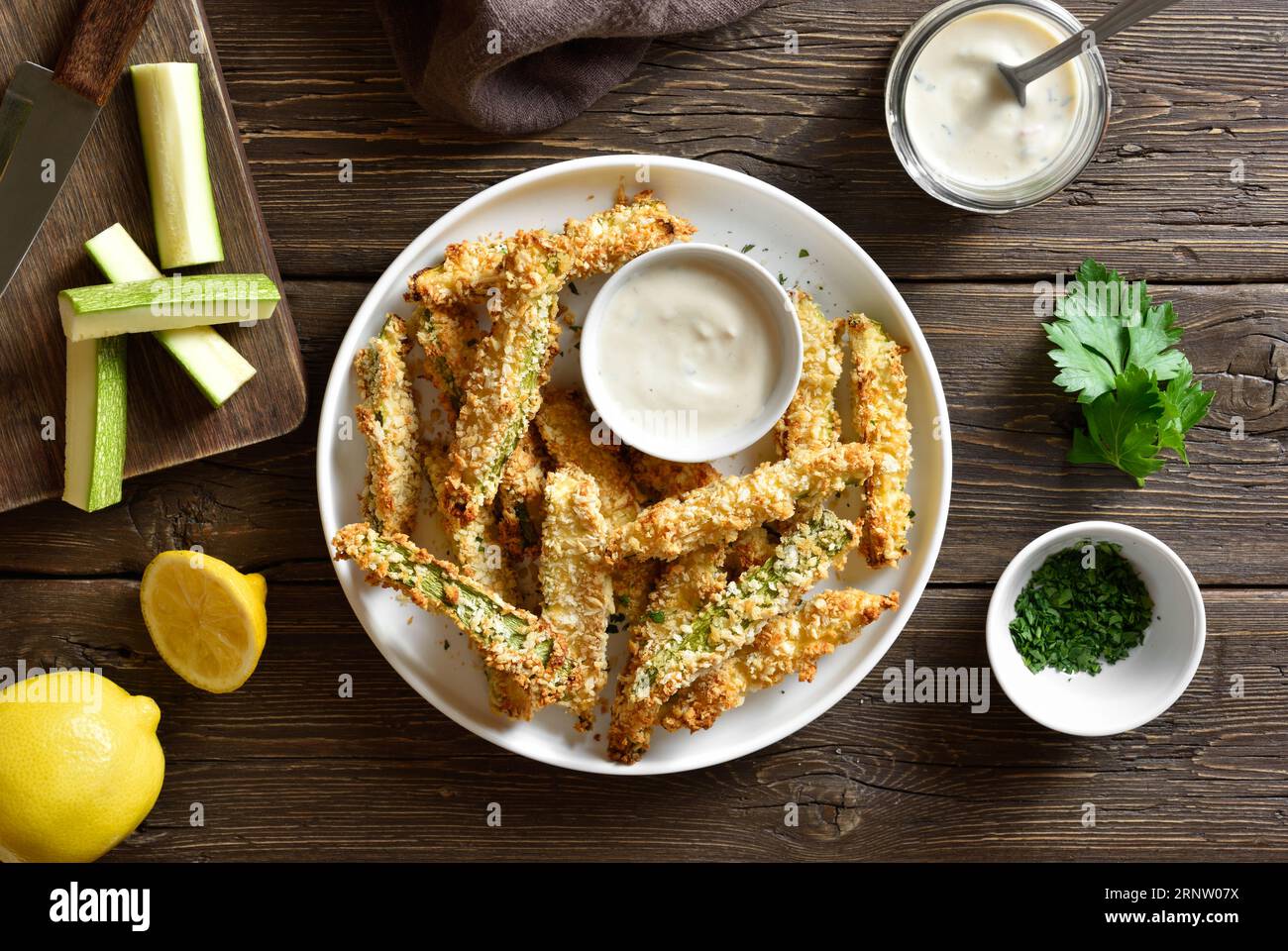 Crunchy zucchini breaded sticks with dipping sauce on plate over wooden background. Top view, flat lay Stock Photo