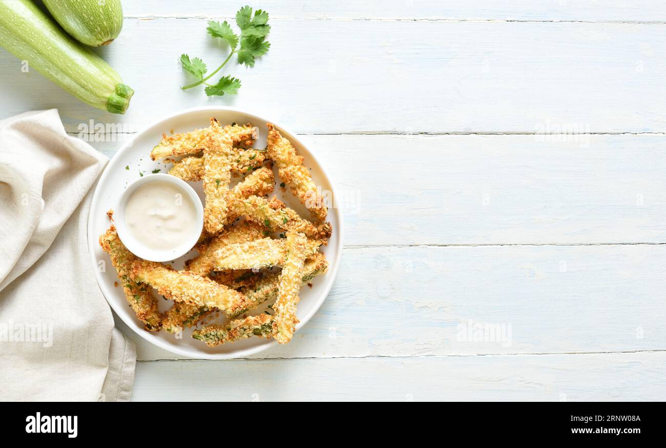 Crispy zucchini fries with dipping sauce on plate over light wooden background with free space. Top view, flat lay Stock Photo
