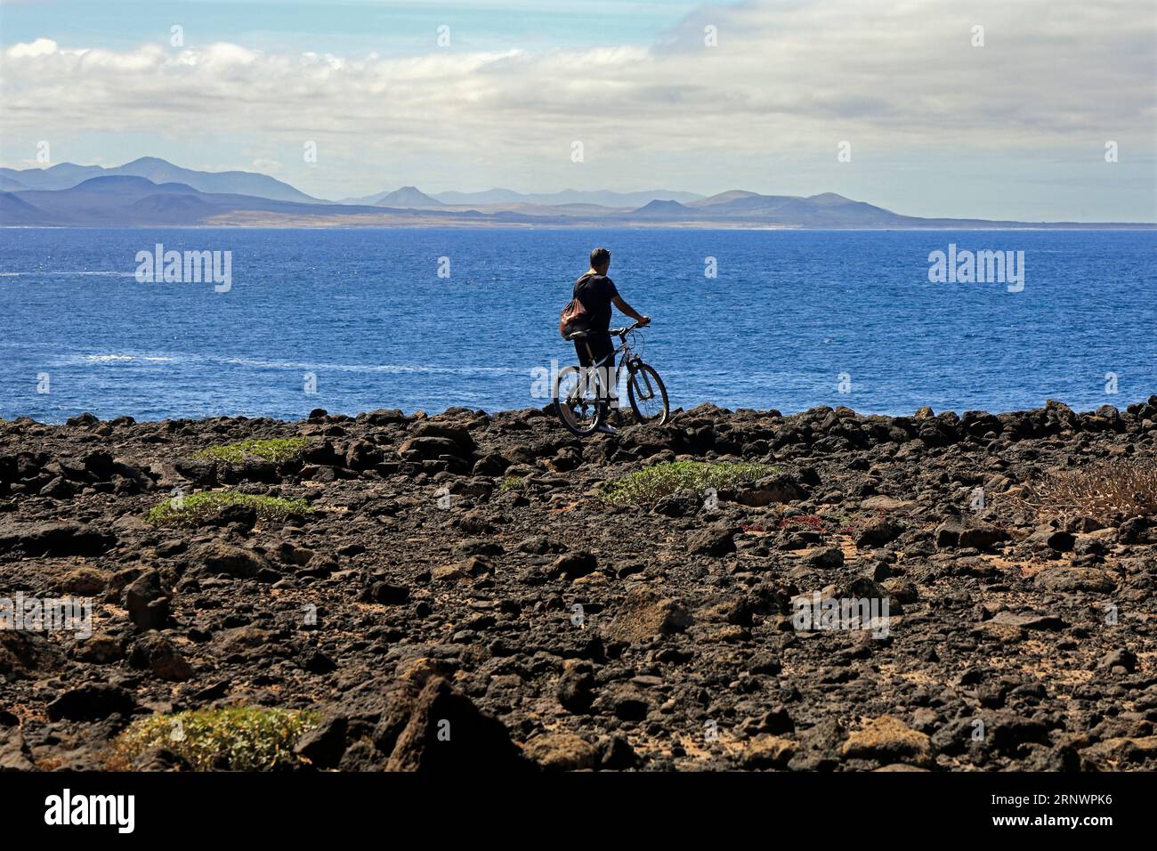 Man on a bicycle looks across towards Fuerteventura on the horizon from Faros area of Lanzarote, Canary Islands, Spain Stock Photo