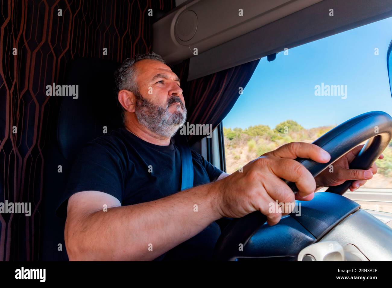 Truck driver driving with both hands on the steering wheel in an alert position. Stock Photo