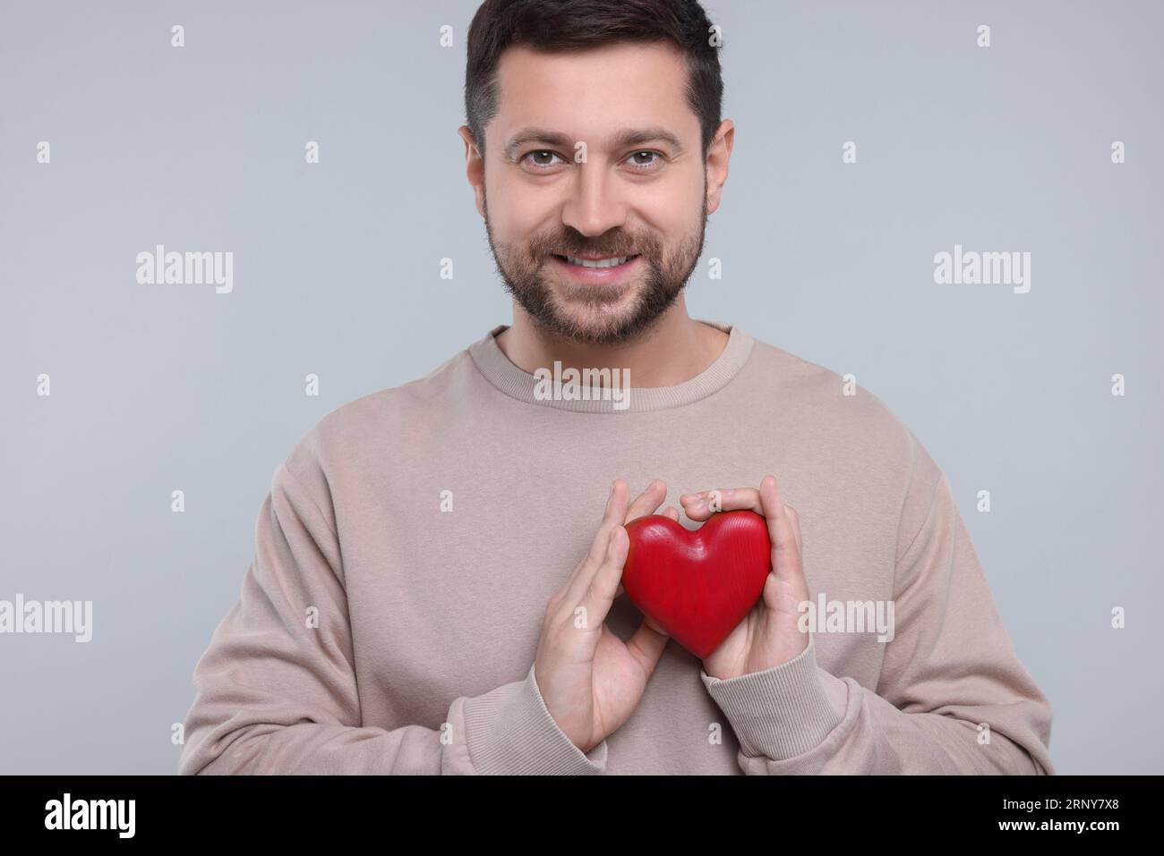 Happy man holding red heart on light grey background Stock Photo - Alamy