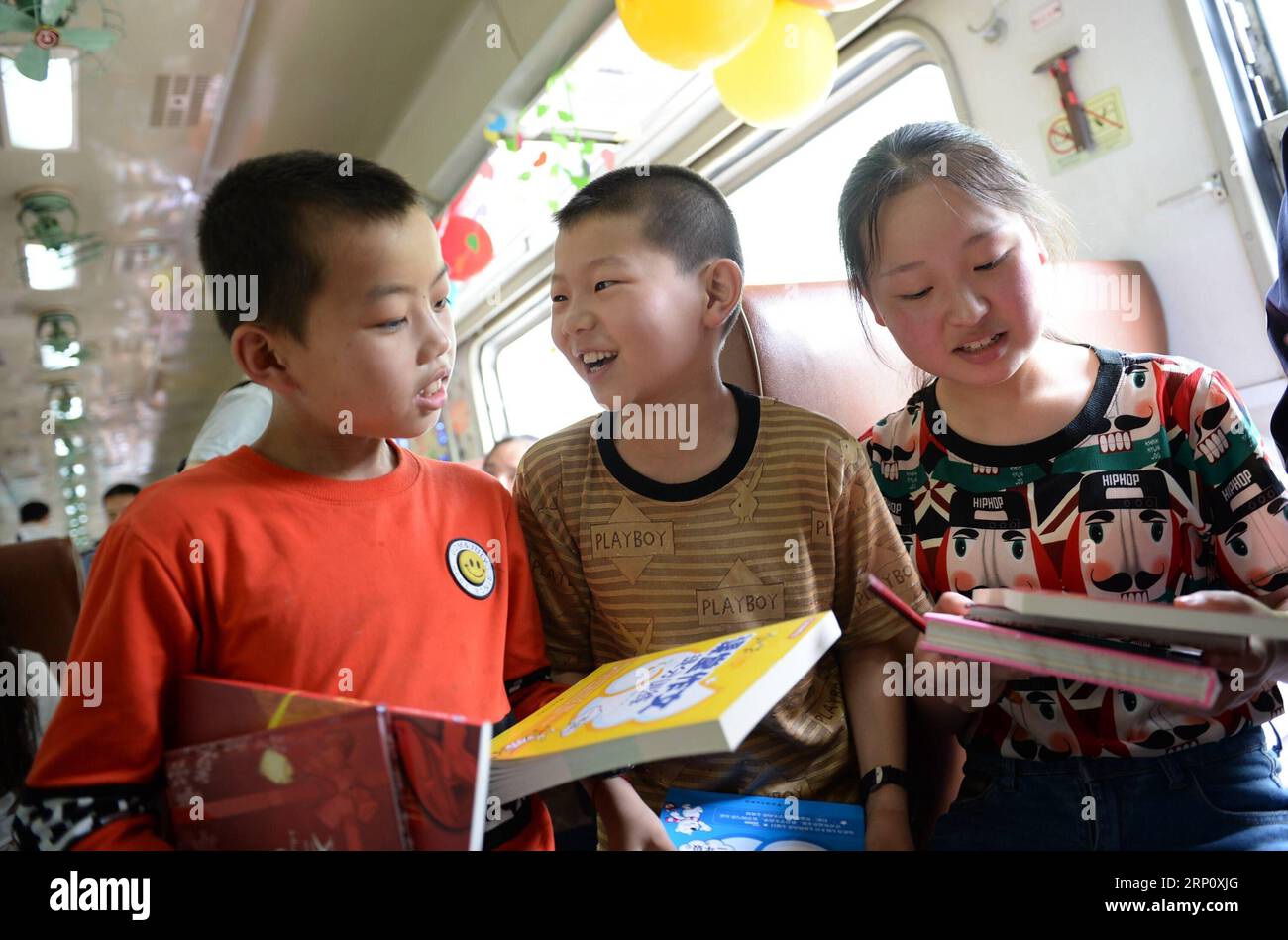 (180529) -- XI AN, May 29, 2018 -- Students receive new books at the students special carriages on train No. 6063 in China, May 27, 2018. The train No. 6063, which links 38 stations along the route from Baoji of Shaanxi Province and Guangyuan of Sichuan Province, serves thousands of students who live in mountainous areas and need to commute from schools to home every week. To improve services to the student passengers, student special carriages installed with bigger desks and a library were put into use at the end of 2017. With the approach of this year s International Children s Day, over 300 Stock Photo