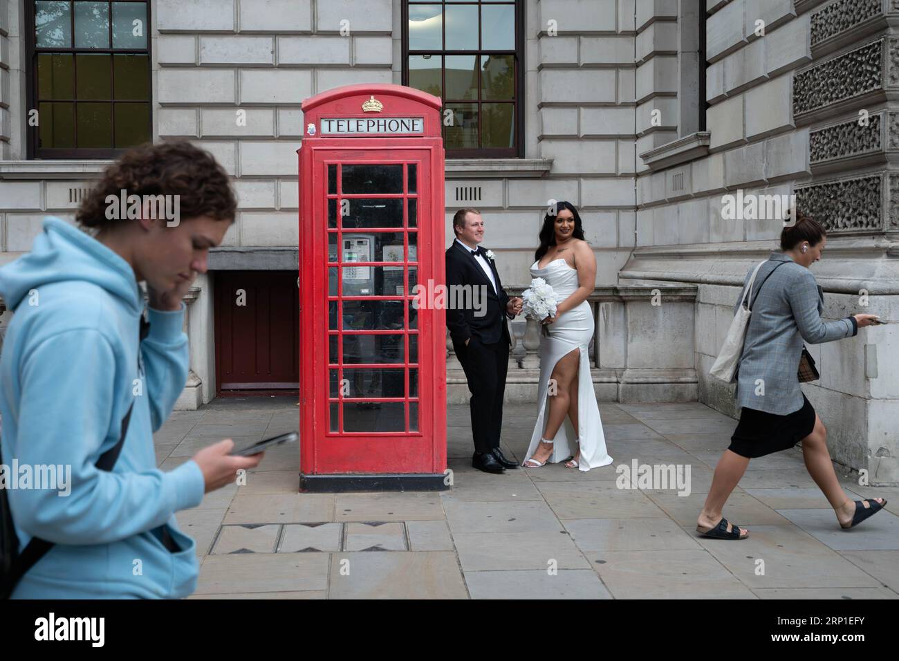 A newly married couple have their picture taken beside a red phone box at Parliament Square in Westminster, as the popularity of the famous booths endures in the social media age as they approach their 100th anniversary. The famous red phone box was designed by architect Sir Giles Gilbert Scott for a competition in 1924. Picture date: Tuesday August 15, 2023. Stock Photo