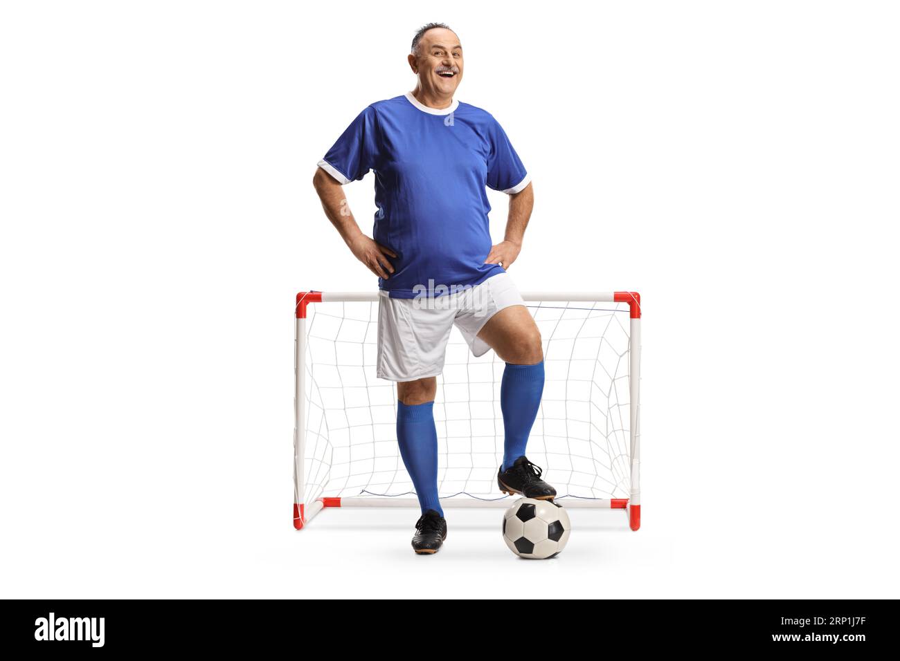 Smiling mature man wearing a football sports jersey and standing in front of a mini goal isolated on white background Stock Photo