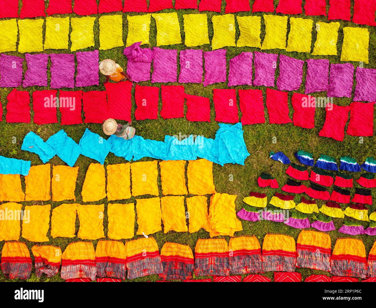 Narayanganj, Dhaka, Bangladesh. 3rd Sep, 2023. Hundreds of pieces of dyed cloth are spread out across a field at Batik Village in Narayanganj, Bangladesh for drying which looks like a Kingdom of Colors. Workers use hats for protection from the scorching heat because they have to constantly turn the colorful fabrics so that they dry perfectly in the sunlight. Beautifully embellished colorful cloths are created using the Indonesian technique called ''Batik''. Parts of the design are blocked out by applying hot wax over them, then a dye is applied on top and the parts covered in wax resist th Stock Photo