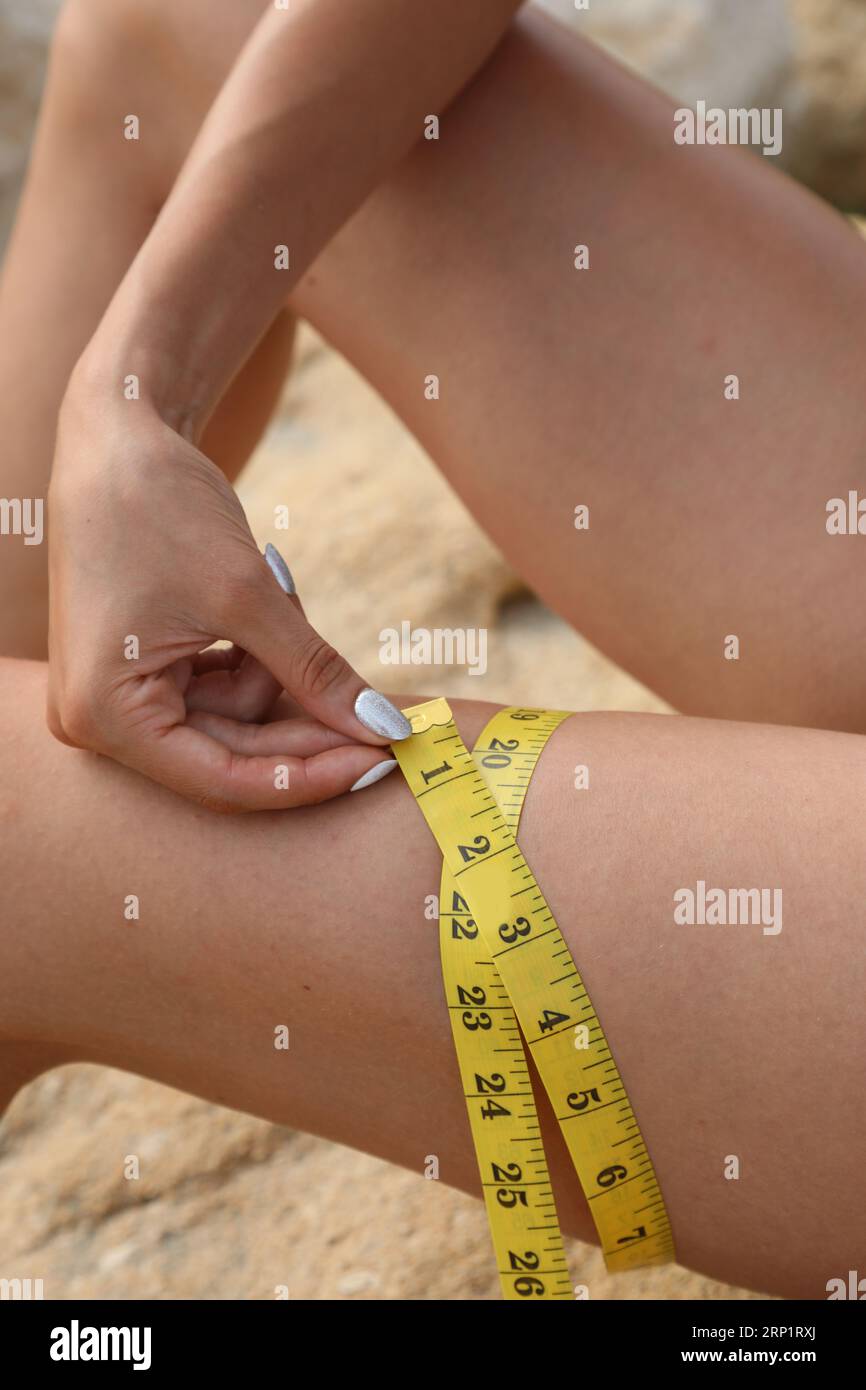 thihg of a slender girl while measuring with yellow meter and measure in inches Stock Photo