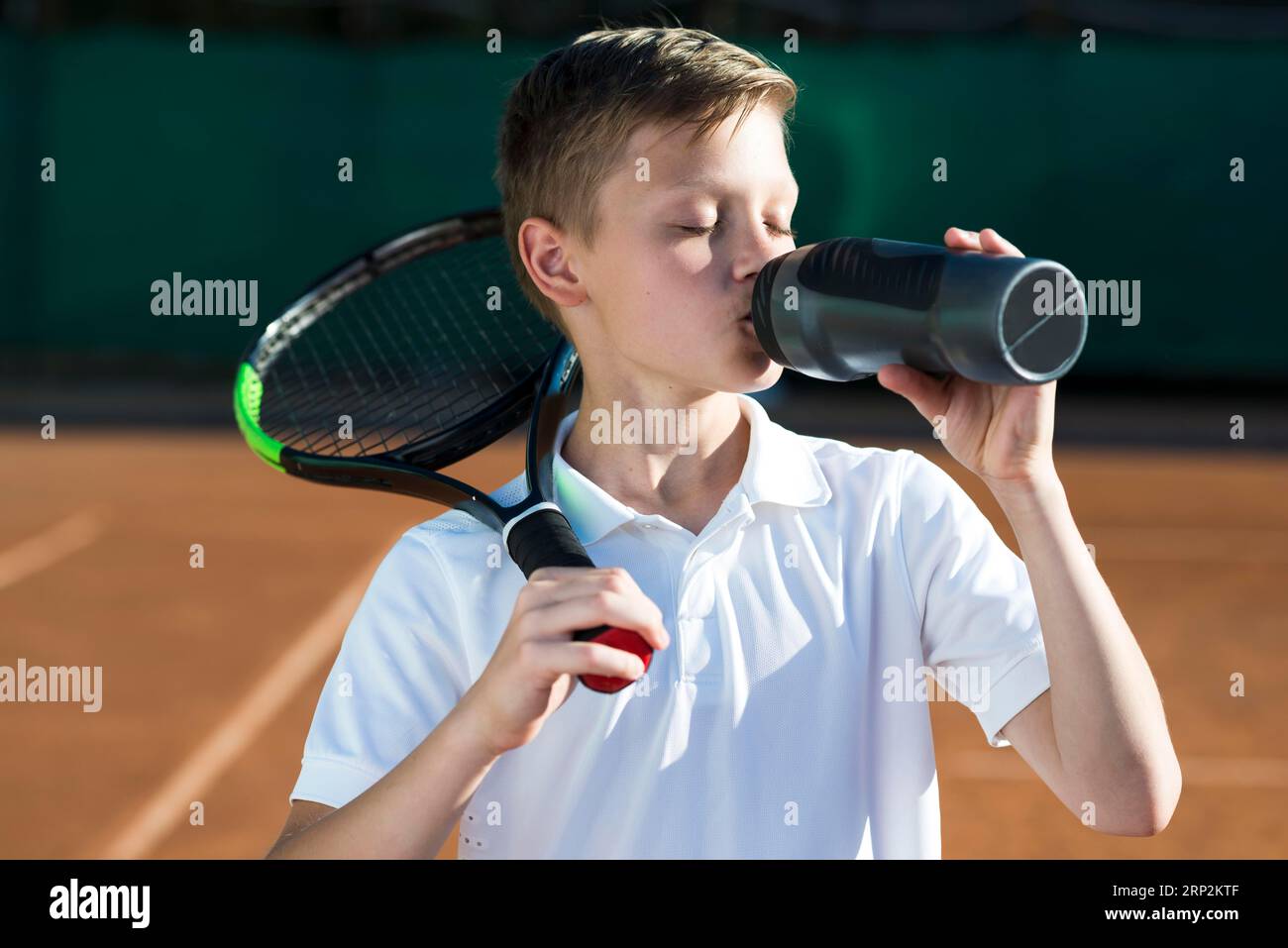 Kid with racket shoulder drinking water Stock Photo - Alamy