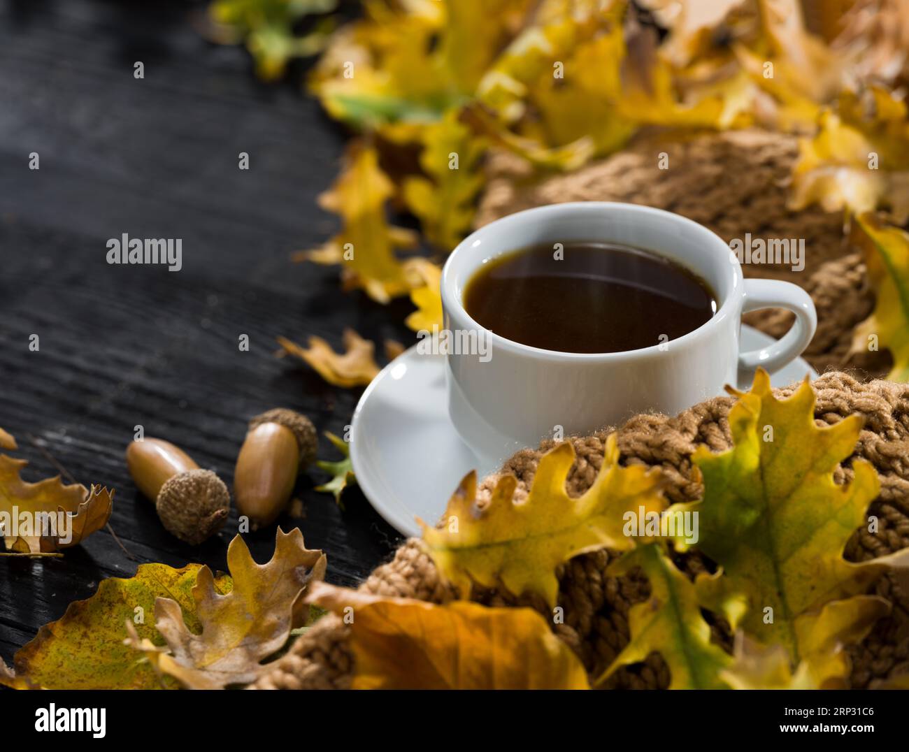 Hot coffee and autumn leaves. Modern coffee mug on black table with autumn coffee concept. Stock Photo