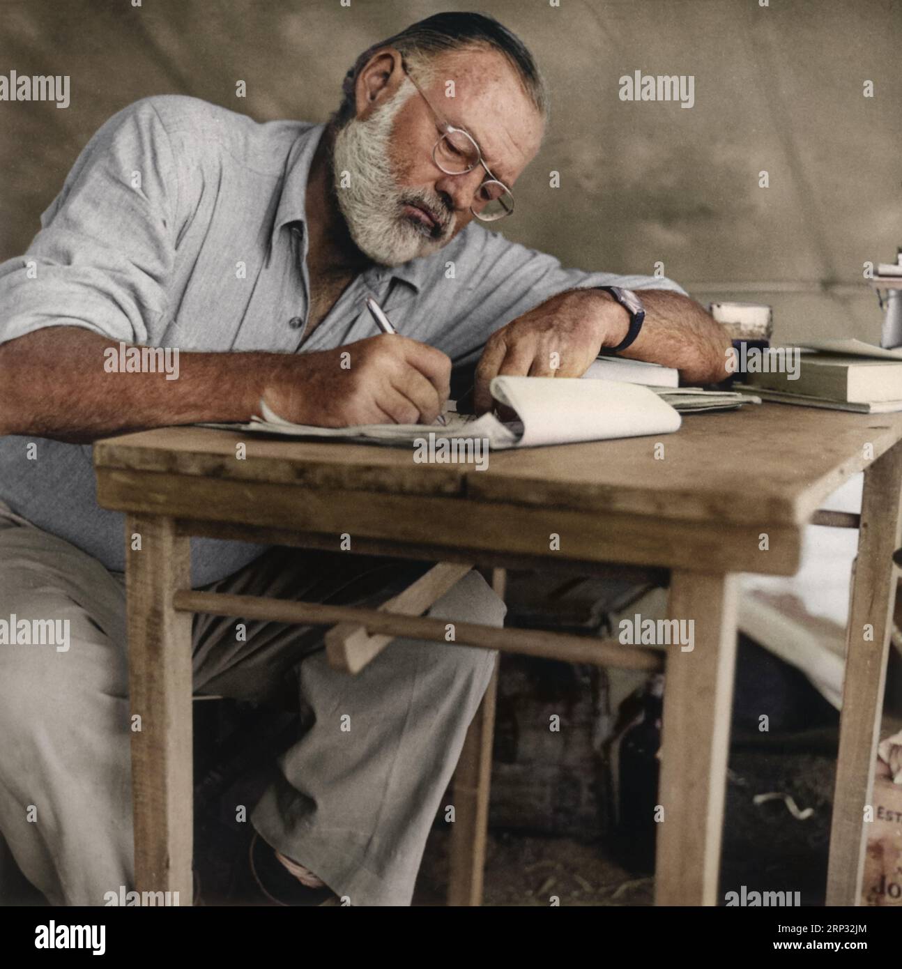 Photograph of Ernest Hemingway sitting at a table writing while at his campsite in Kenya circa 1953. Stock Photo