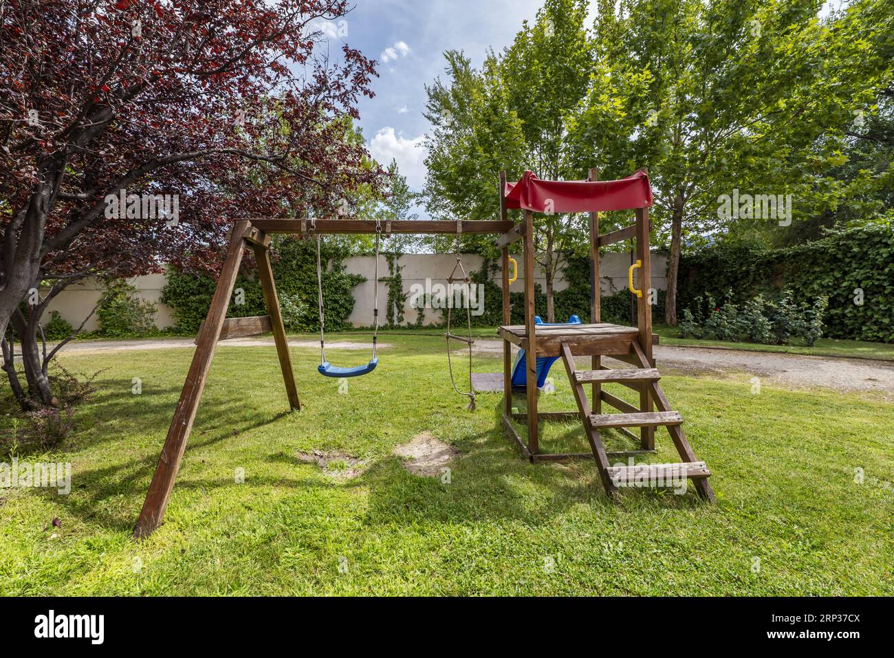 A wooden swing along with a slide on the grass of a garden in the common area of an urbanization Stock Photo