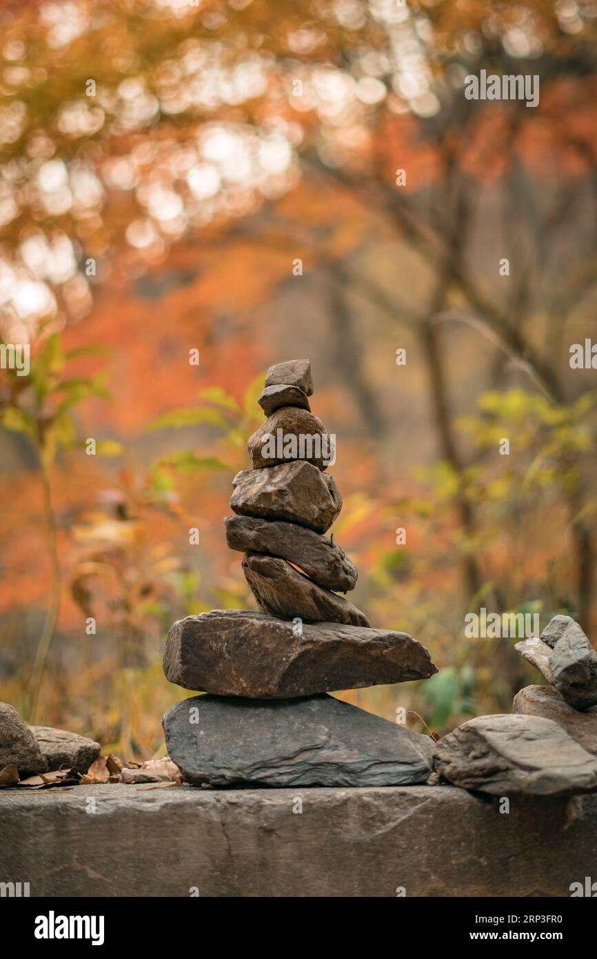 Zen stones stacked and piled on each other showing delicate balance of nature amidst foliage trees; it symbolizes prayer and marks hiking route trails Stock Photo