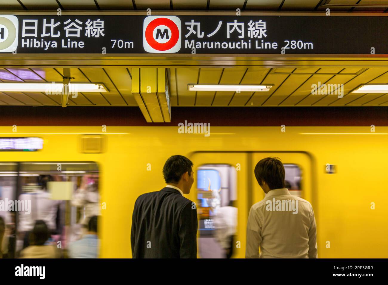 Tokyo, Japan - 22 June 2023: Commuters wait for a JR Lines underground train from a Tokyo metro station. Selective focus on signage for Marunouchi and Stock Photo