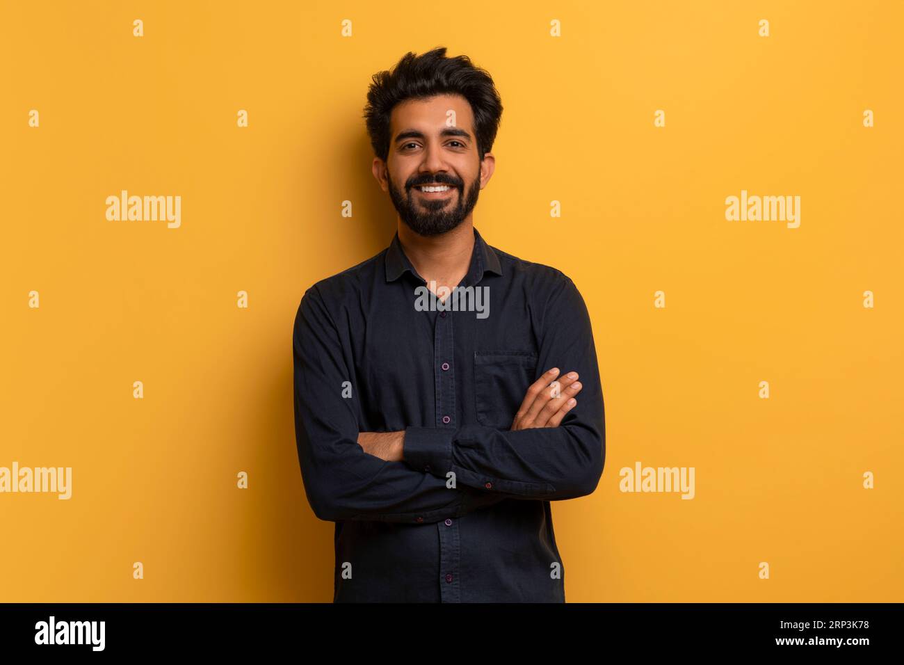 Confident young indian man standing with folded arms over yellow background Stock Photo