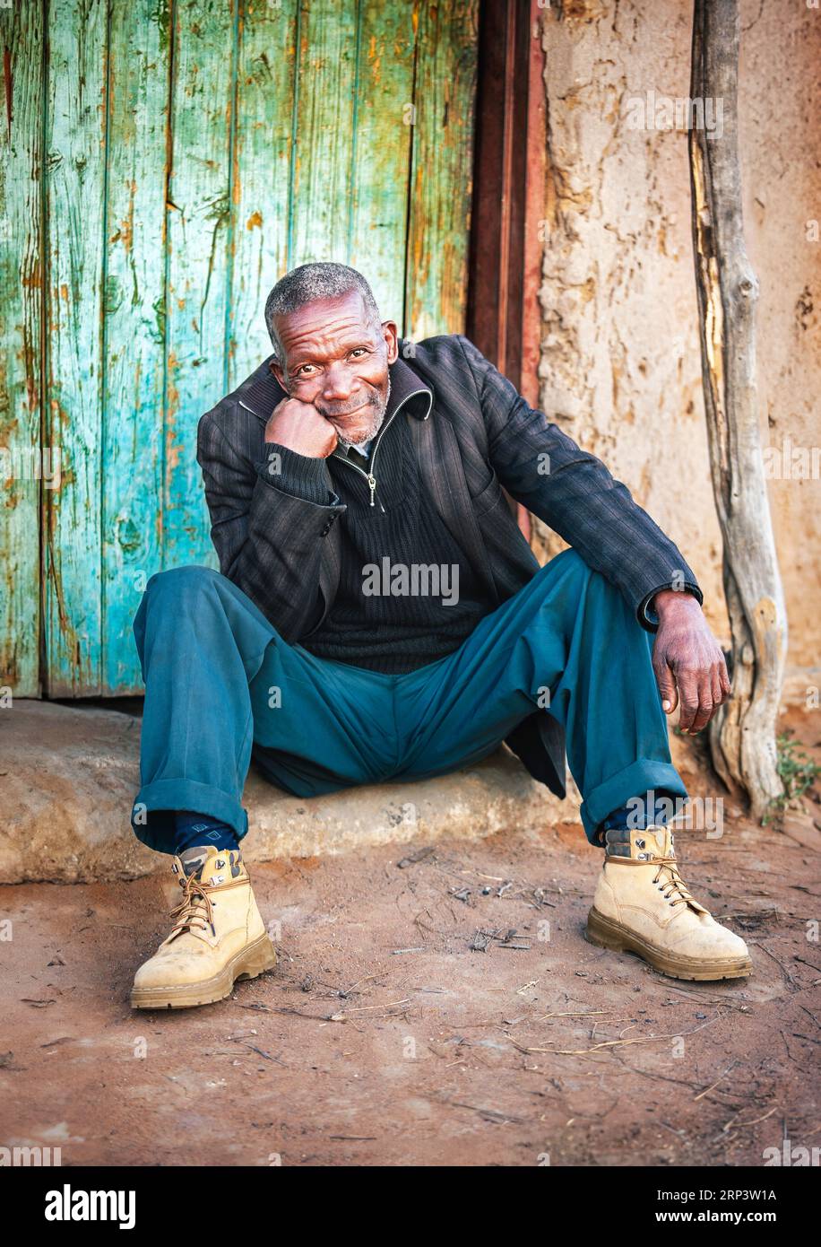 old african villager portrait sited on the doorstep ,outdoors in the yard of his home Stock Photo