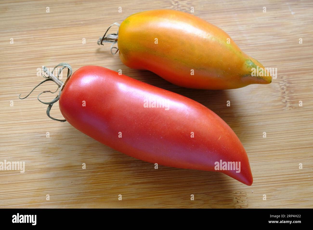 Pair of Witch Nose Long Tomatoes on wooden chopping board Stock Photo